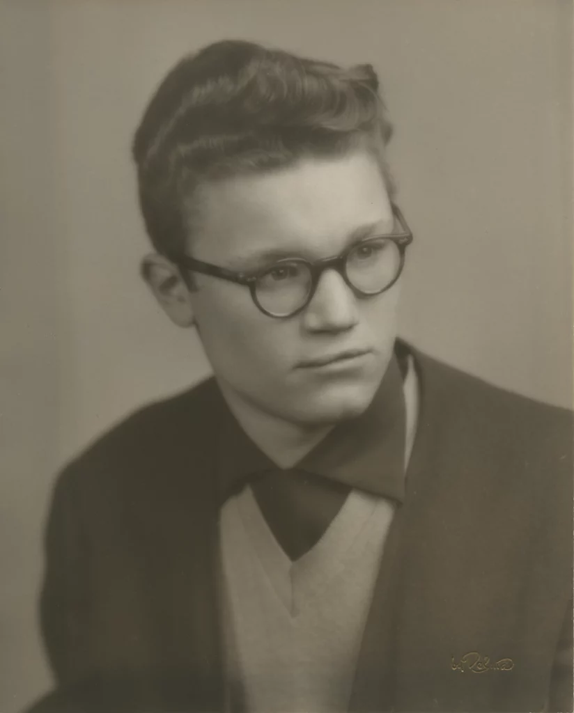 Black and white portrait photograph from the 1950s of a young, light-skinned man with round glasses.