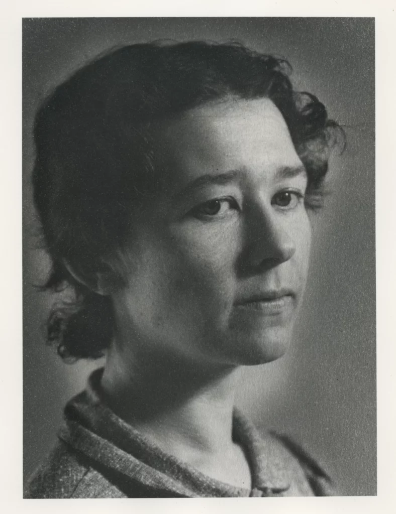 Black and white portrait from the early 1930s of a woman with a light skin tone and short, curtly hair, lowering her gazing past the photographer.