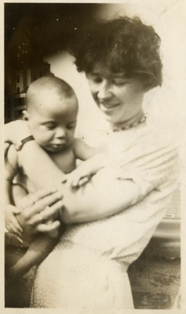 Black and white photograph of a women with short hair holding a baby in her arms, both with light skin tones.