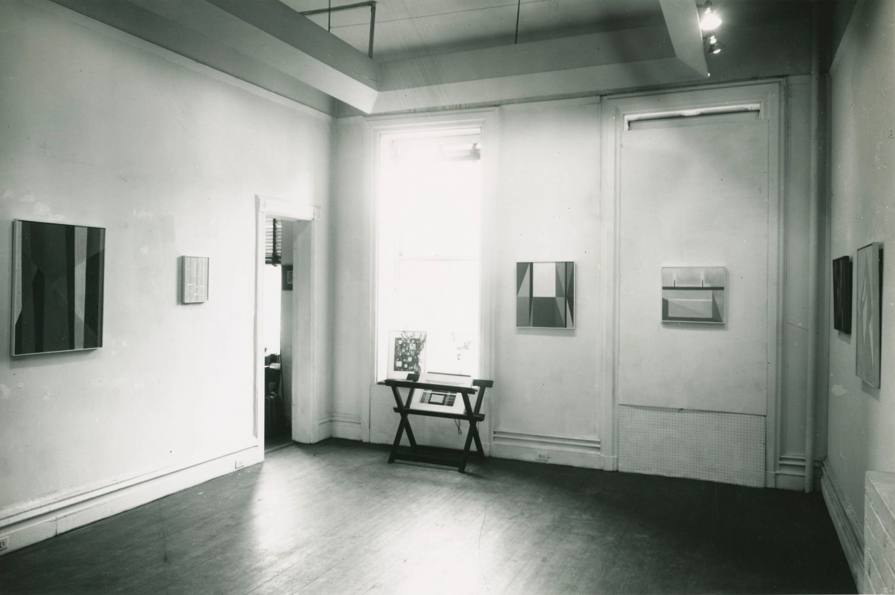 Black and white photograph from 1959 of a gallery interior, with six canvases displayed over three walls, and a window with a small display of prints in front.