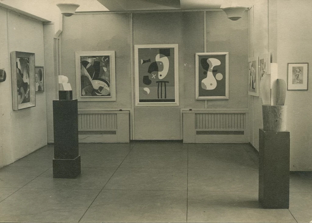 Black and white photograph from 1937 of an exhibition space with abstract artworks on the walls, and two abstract sculptures on pedestals.