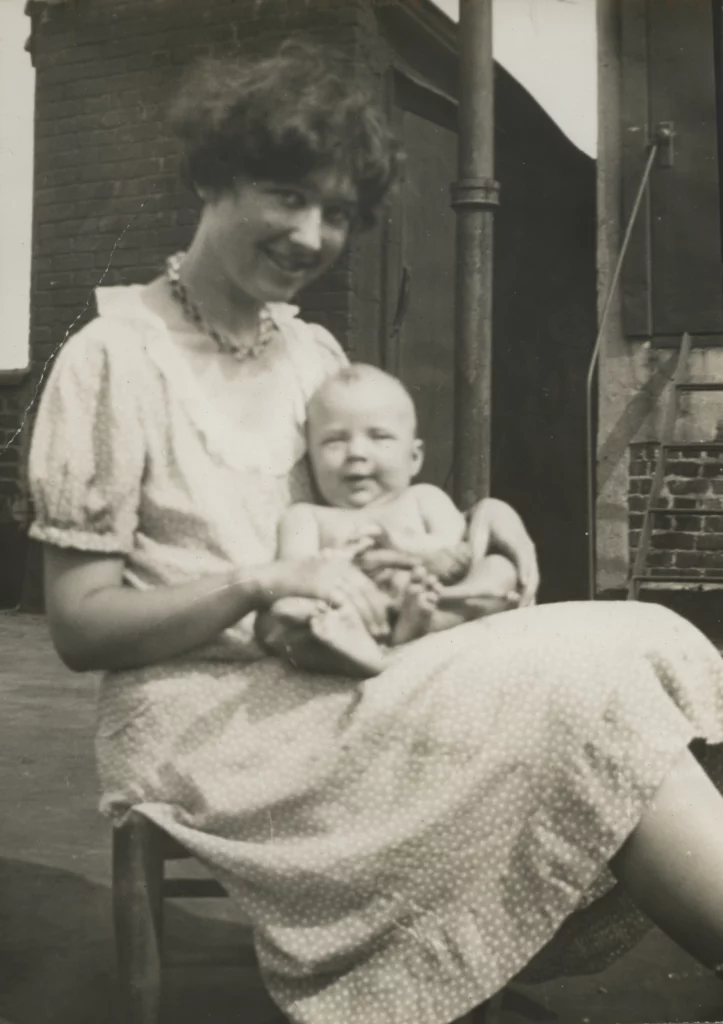 A black and white photograph from 1932 of a woman with a light skin tone wearing a dress, seated, and holding a baby with a light skin tone.