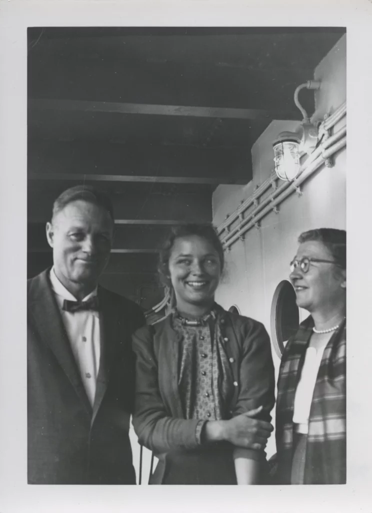 Black and white photograph of a man, young woman, and an older woman on a ship, all with light skin tones and smiling.