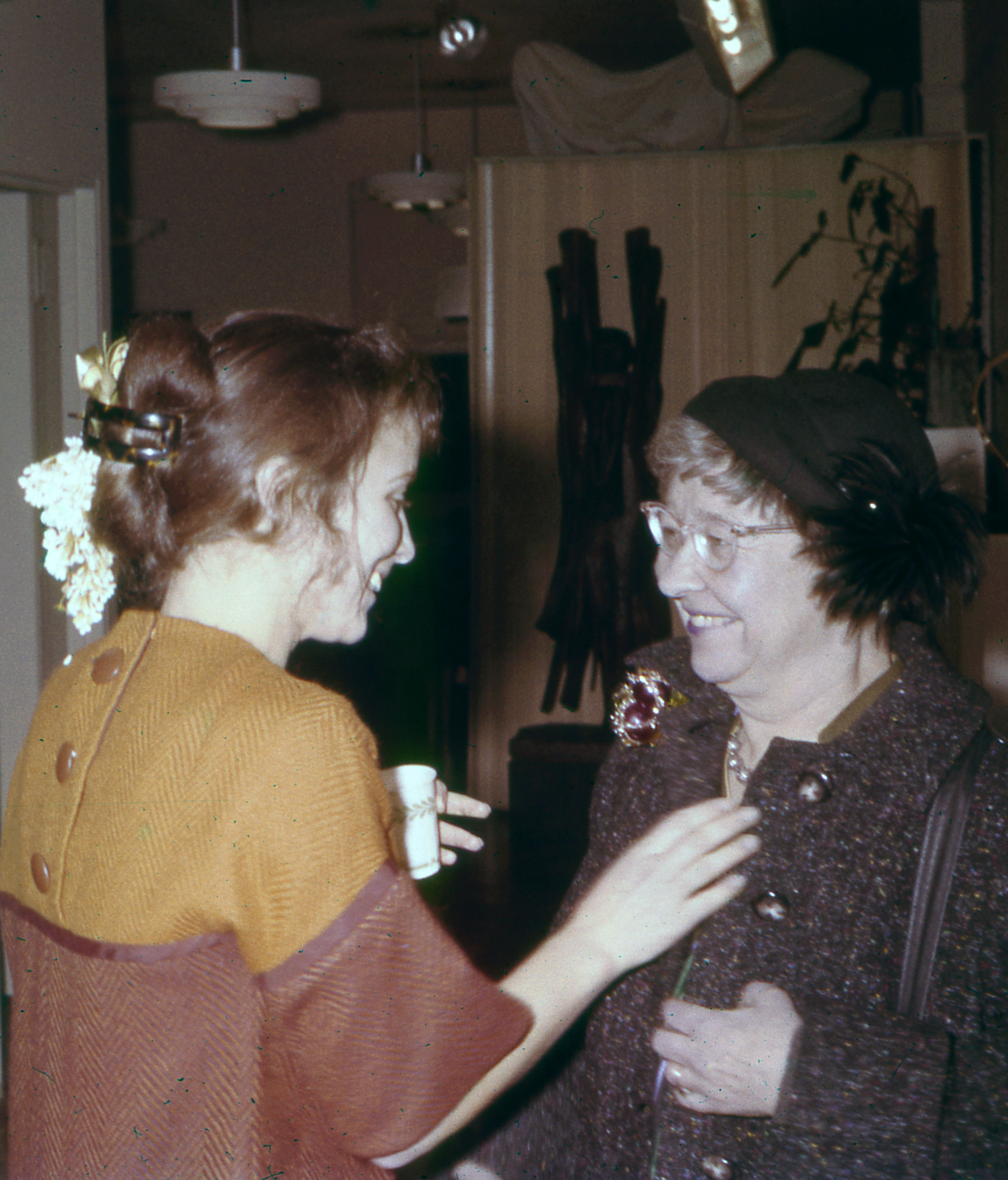 Photograph from the 1960s of two women with light-beige skin, one older and the other younger, conversing in business-causal attire