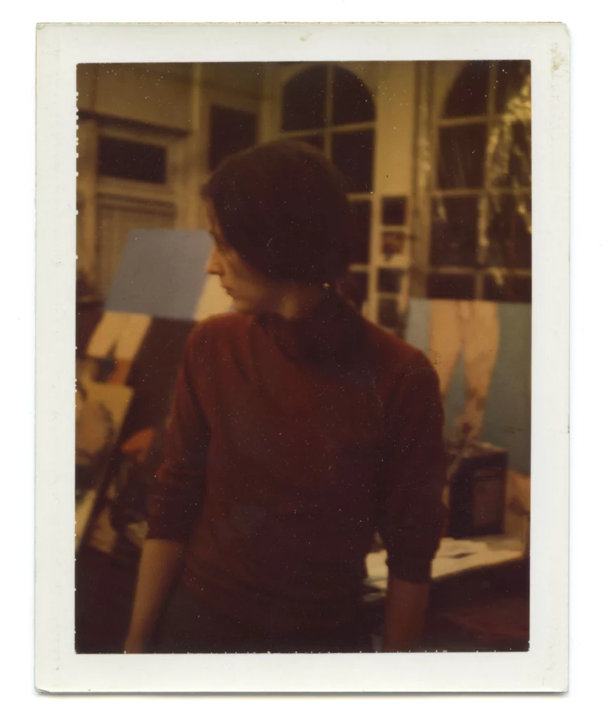 Photograph from the late 1970s/early 1980s of a woman with a beige skin tone and brown ponytail wearing a burgundy turtleneck, inside of a classroom studio.