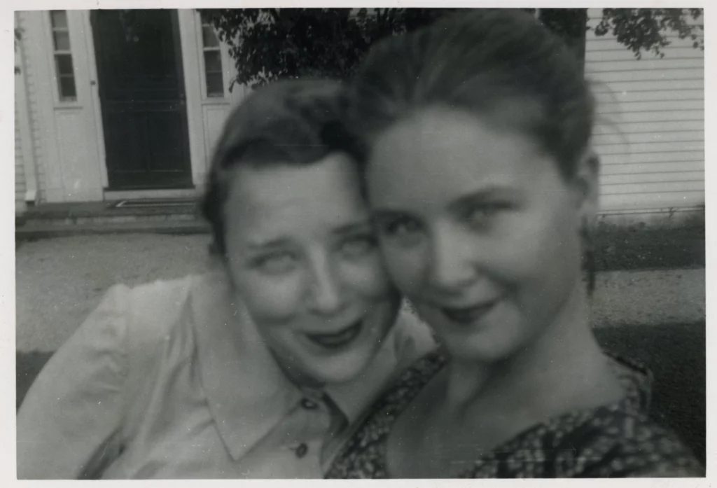 Black and white selfie photograph from the 1950s of two woman with light skin tones, their heads next to each other, looking into the camera.