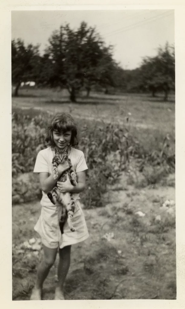 Sepia toned photograph from 1941 of a light-skinned girl holding a cat in a pastoral setting.