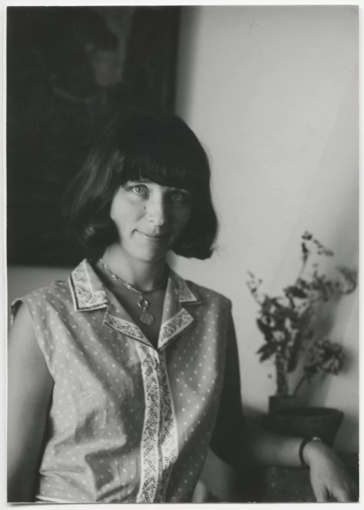 Black and white photograph from 1964 of a woman with a light skin tone and a bob haircut with bangs, seated, looking directly at the camera.
