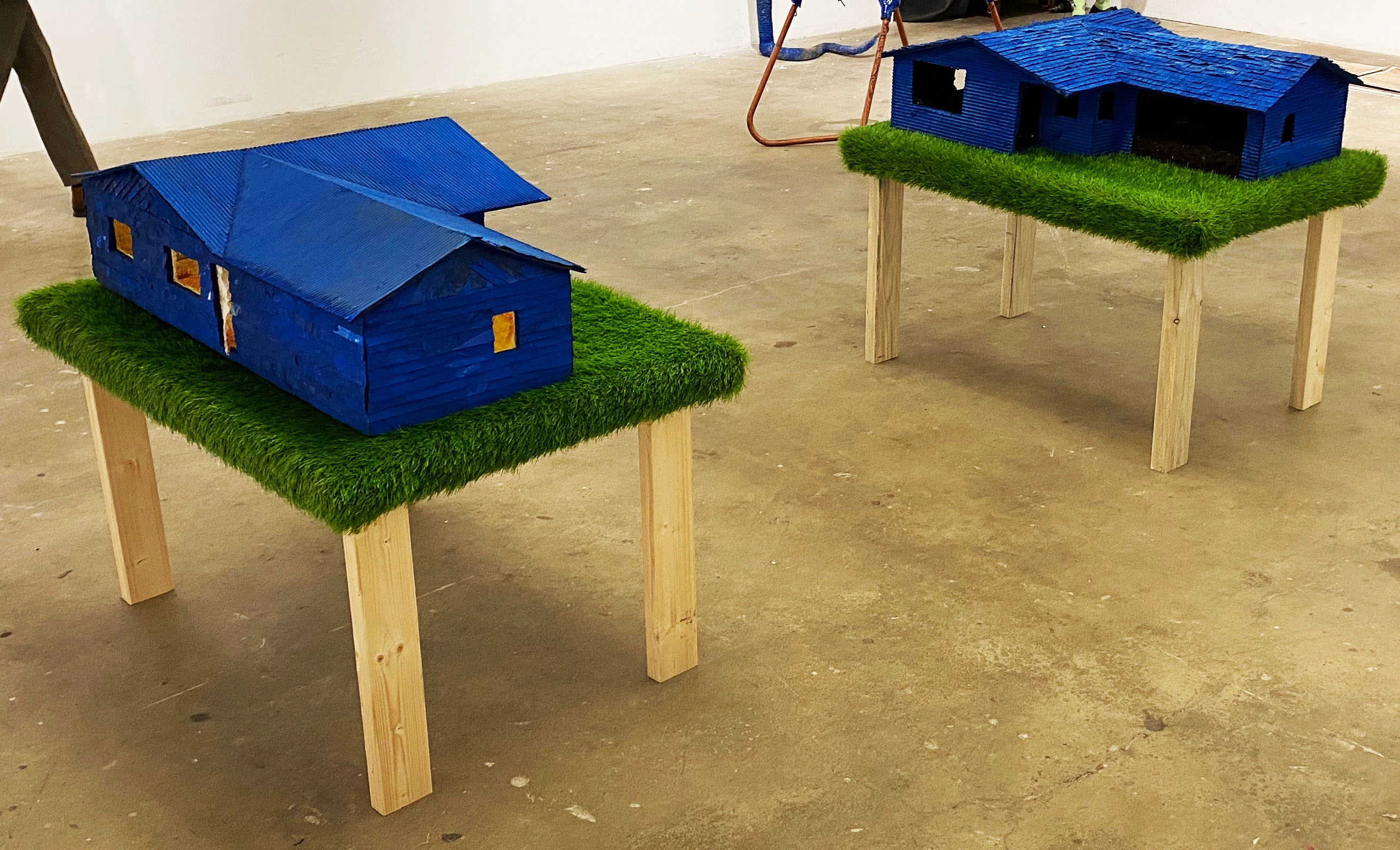 Photograph of two tables with blue model houses on top of green astroturf.