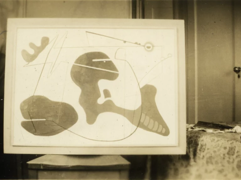 Sepia-toned photograph from the early 1940s of a biomorphic painting on an easel. A door in the background and a floral-pattered fabric to the right suggests a domestic interior.