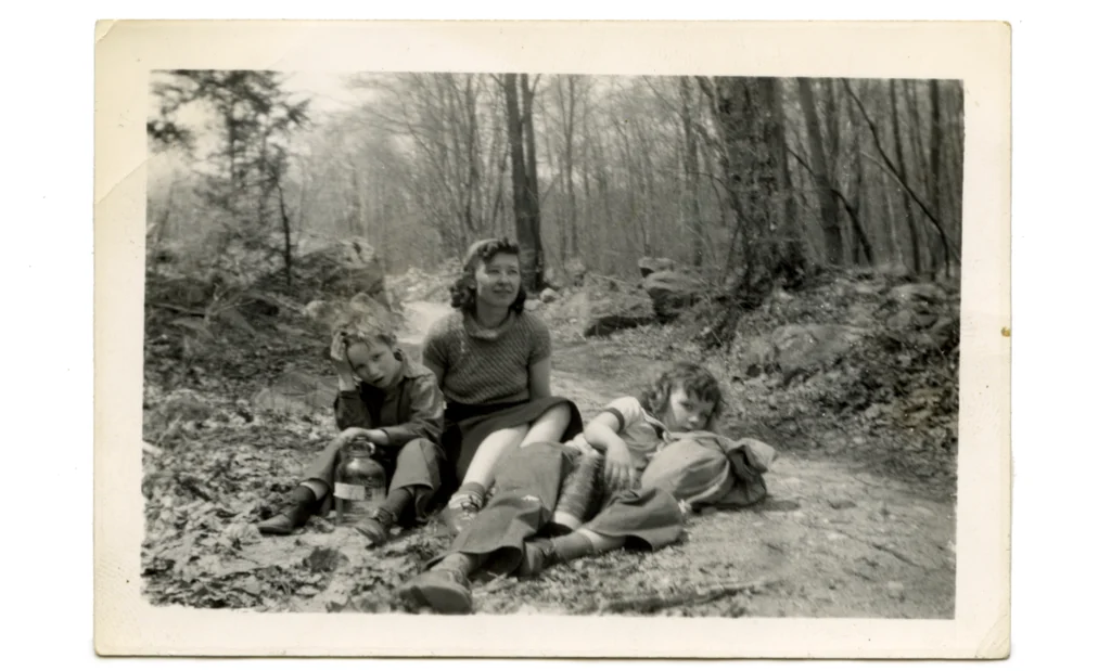 A black and white photograph of a woman and two children beside her, sitting on a path in the woods.Alice Trumbull Mason with Emily and Jo Mason ca. late 1930s. Photography by Ibram Lassaw © 2025 Emily Mason | Alice Trumbull Mason Foundation/ARS.