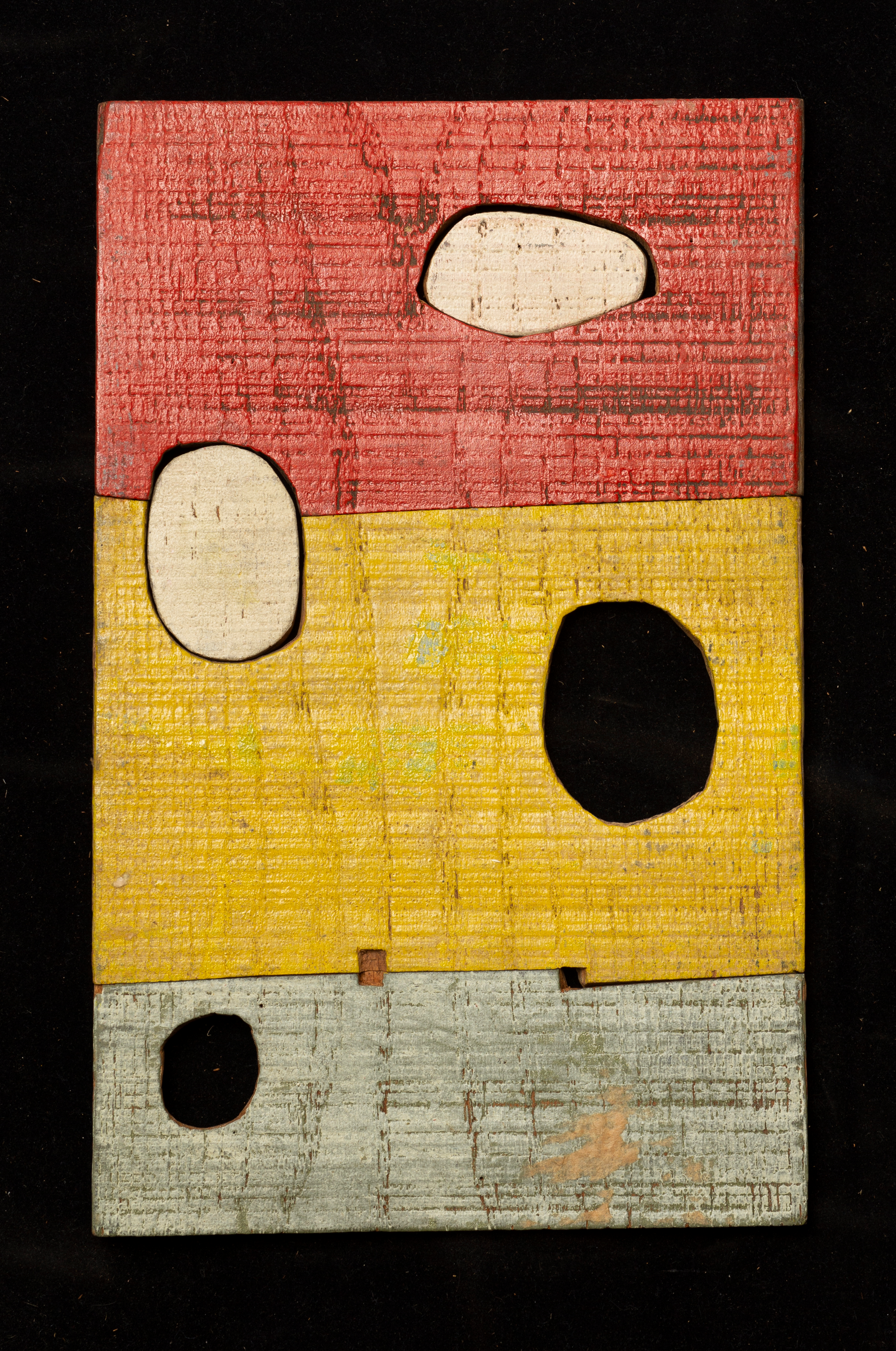 ATM-1955_OBJ_01 Image of a red, yellow, and grey wooden block carved with curved lines and four imperfect circles of varying size cut out.