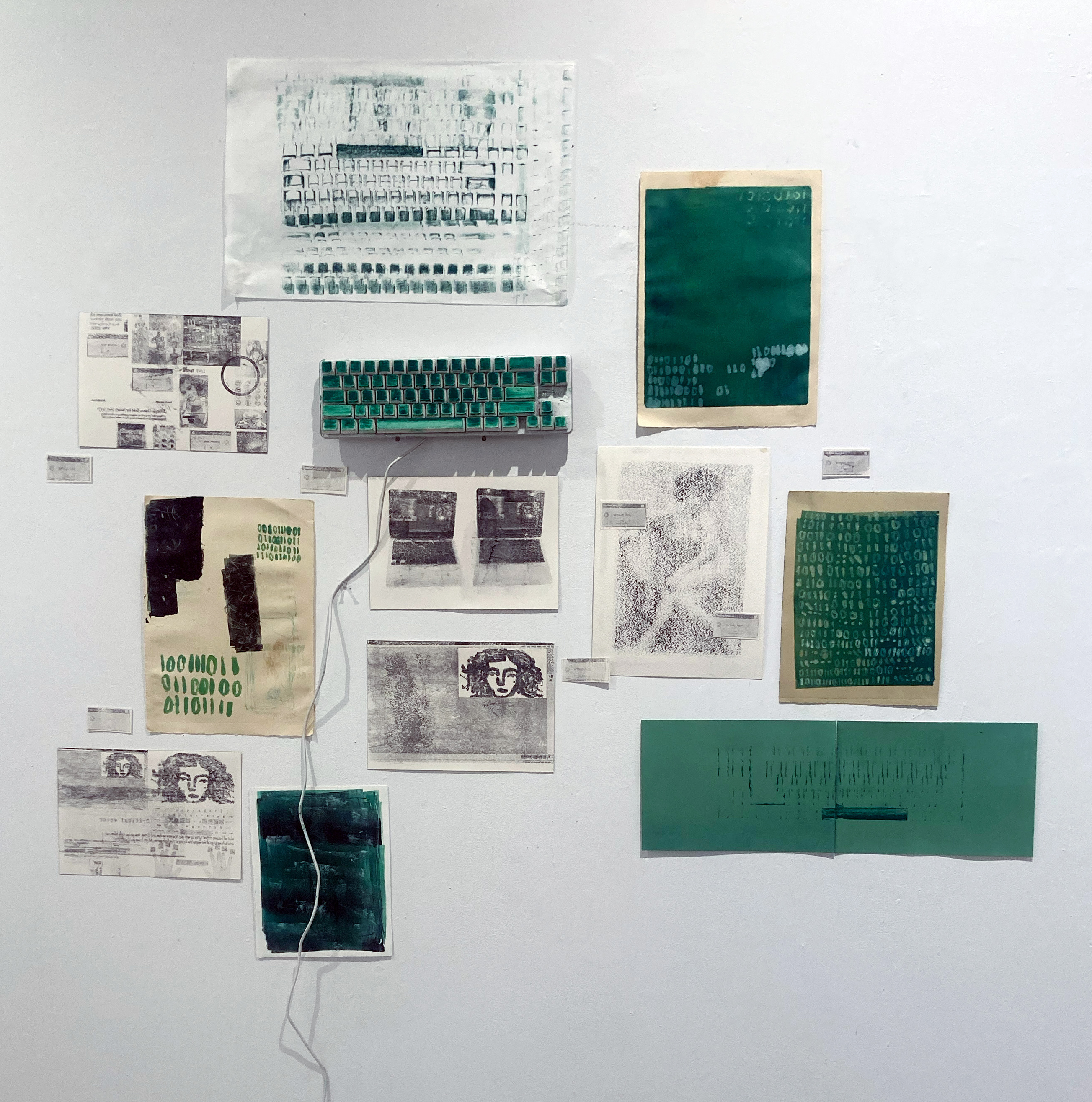 A wall display of drawings, collage, prints, and various mixed media work; green is the predominant color in the installation.