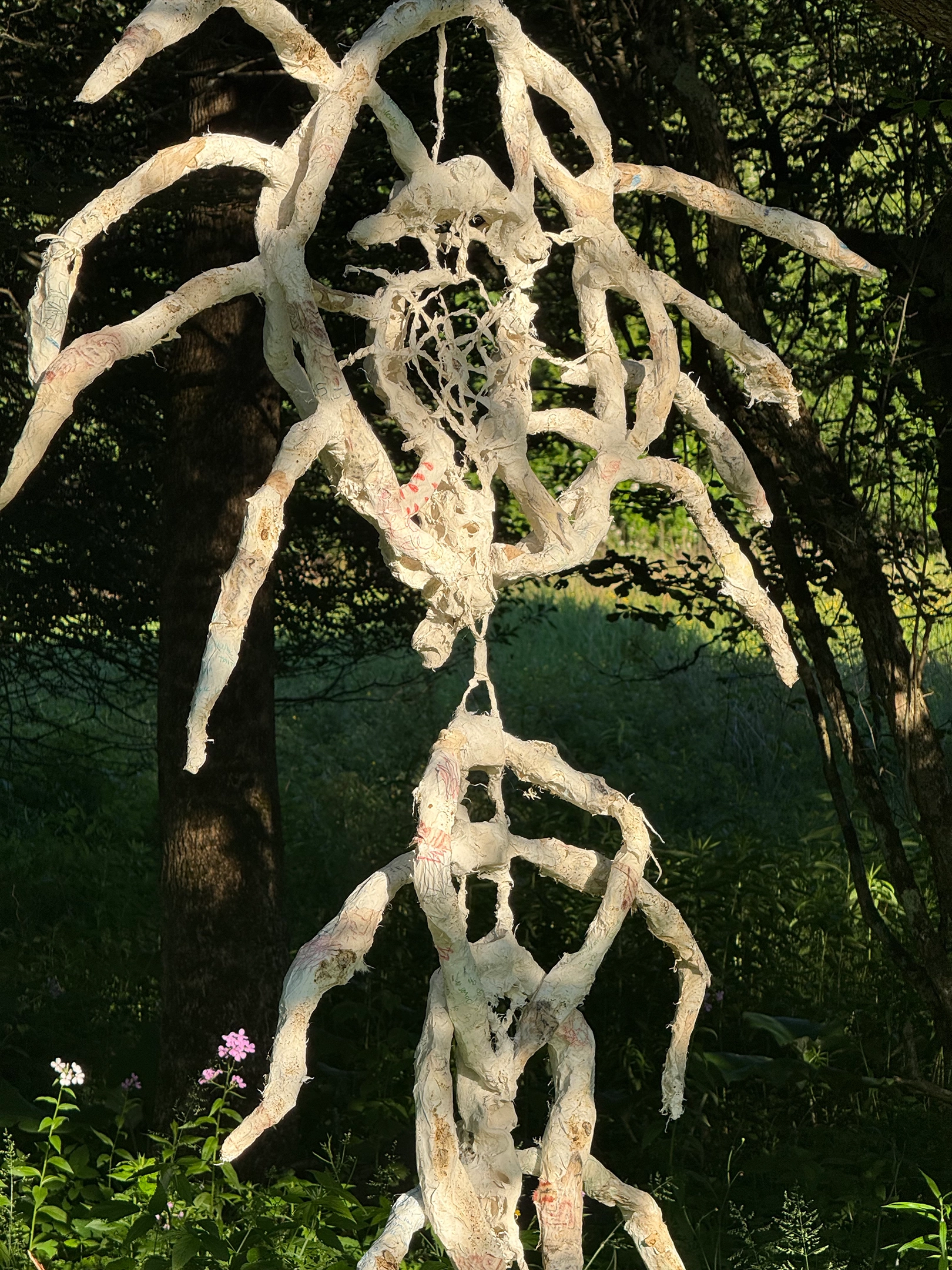 An image of a white, abstract sculpture hanging in a forest.