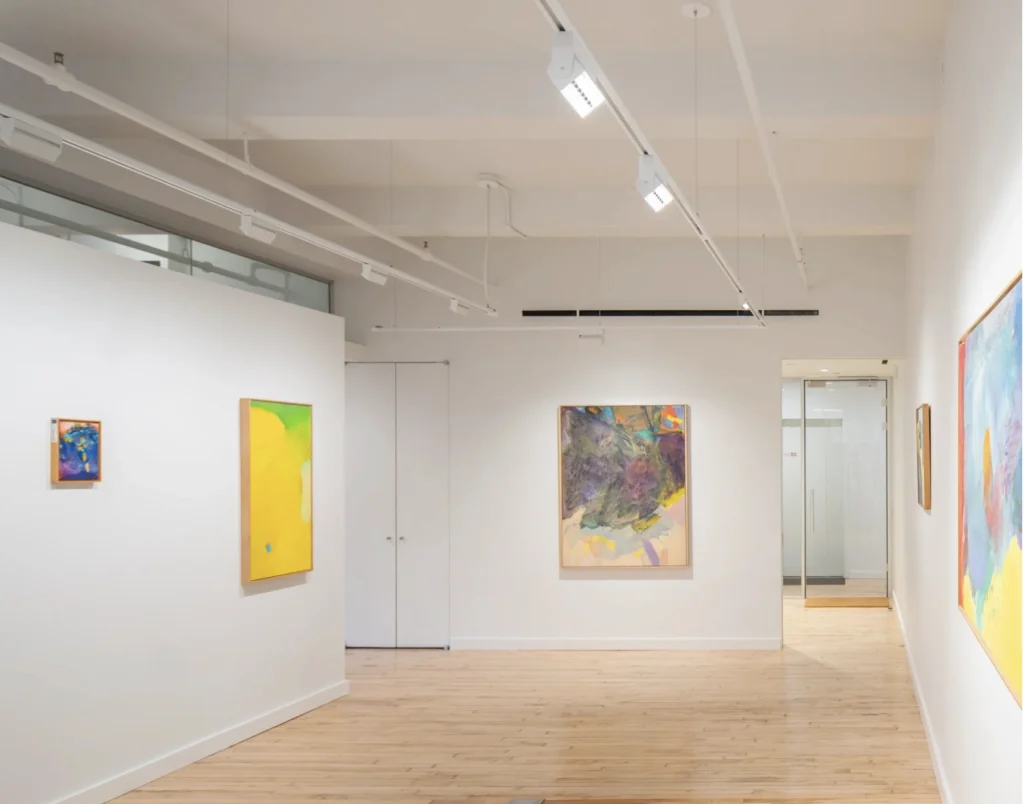 An image of the interior of an office space with light wood floors, white walls, and colorful abstract paintings on the walls.