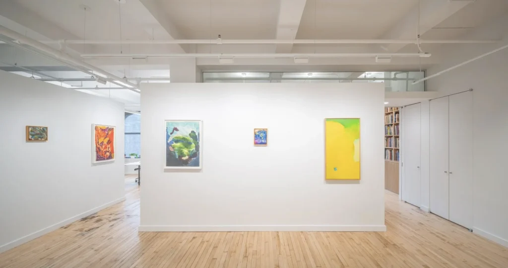An image of the interior of an office space with light wood floors, white walls, and colorful abstract paintings on the walls.